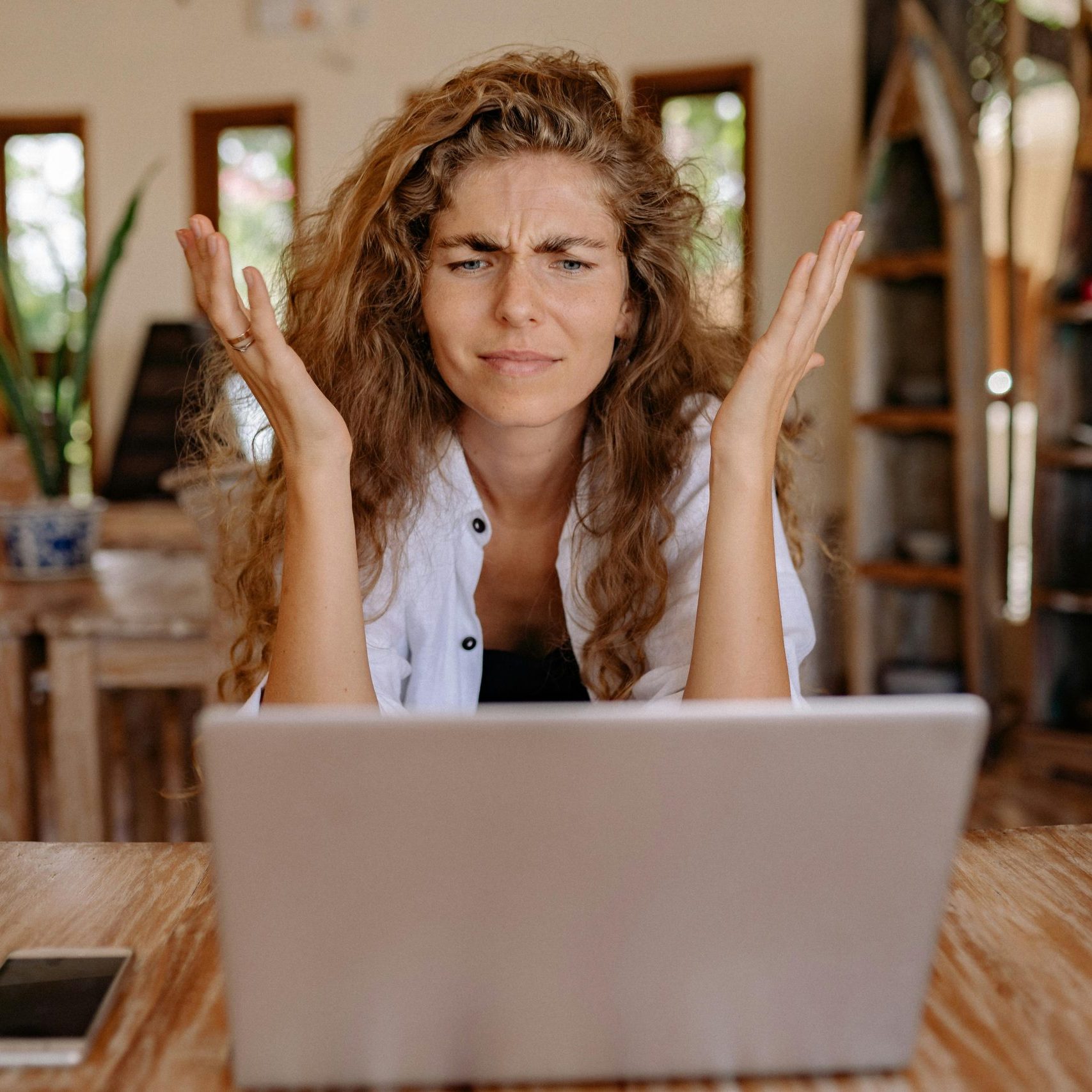 A woman frustrated with her laptop while working remotely indoors, expressing stress.